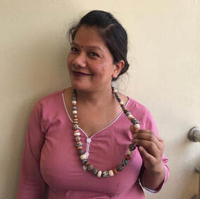Woman in Nepal smiles wearing pink top and bead necklace she has made.