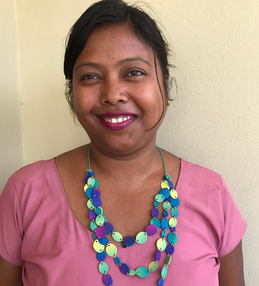 Woman in Nepal smiles wearing pink top and bead necklace she has made.