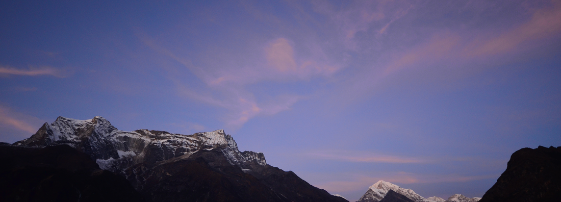 Snow capped mountains and a blue sky with pink clouds at sunrise in Nepal